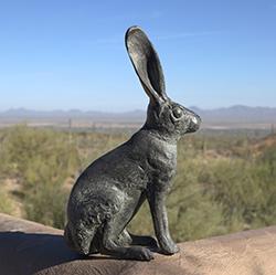 Jackrabbit bronze sculpture sits on an adobe wall with desert landscape and blue sky as background